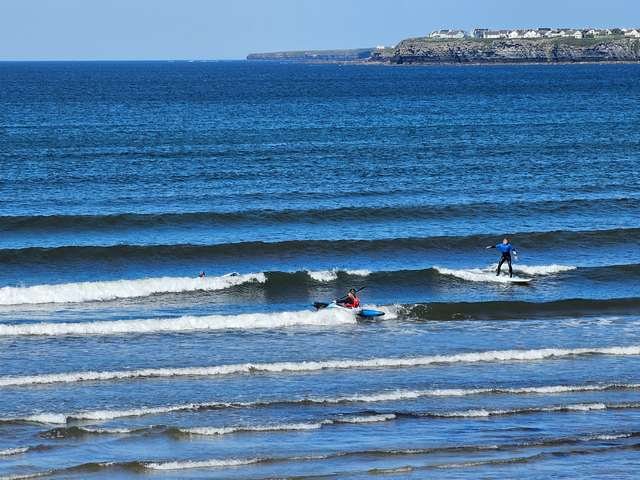 Surfer on a knee high waves in front of Vaughan's on the Prom as a kayaker paddles out the back